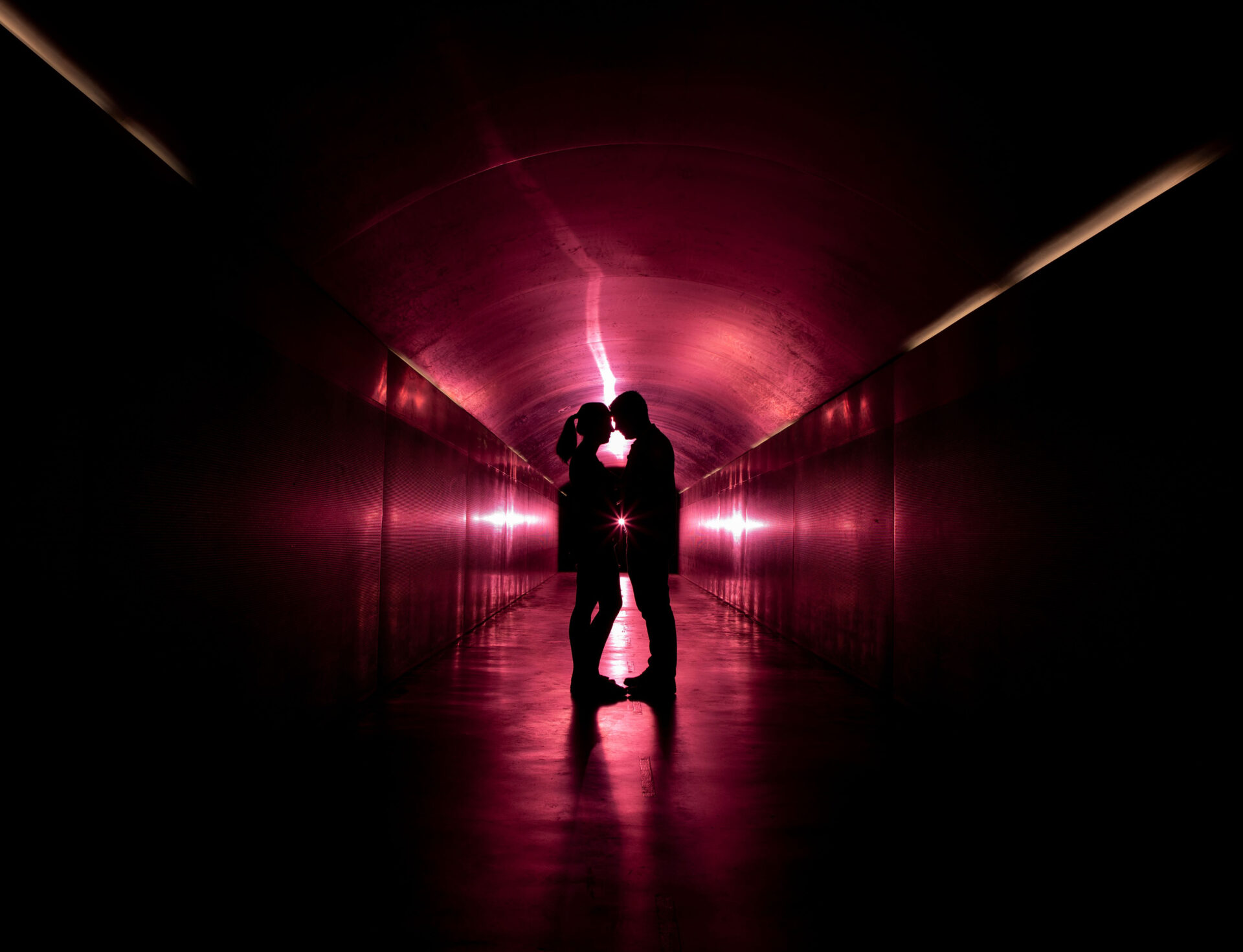 Pareja de novios abrazados en un pasillo iluminado con luces rosas