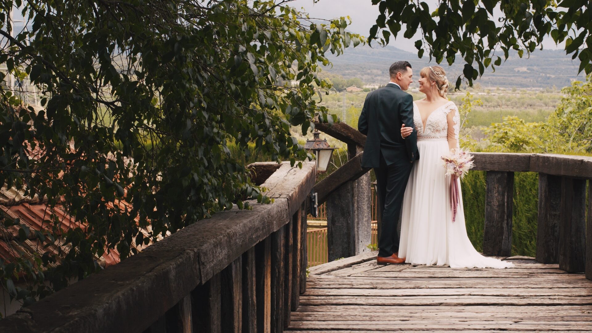 Novios abrazados sobre un puente de madera con paisaje de fondo