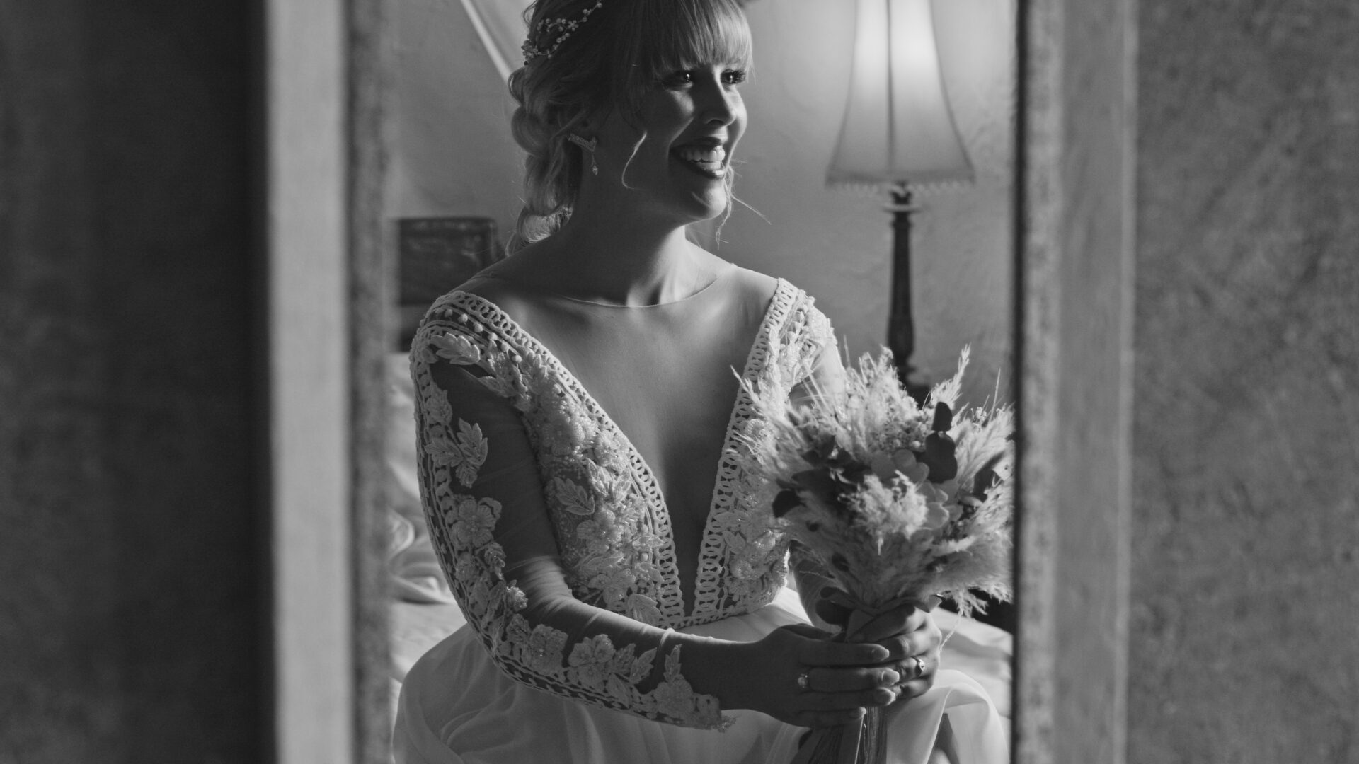 Novia en bata blanca sentada mientras se arregla frente al espejo.